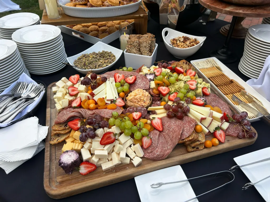 Luxurious fall charcuterie board featuring salami, artisan cheeses, red and green grapes, strawberries, and kumquats, set on a dark linen at a wedding reception.