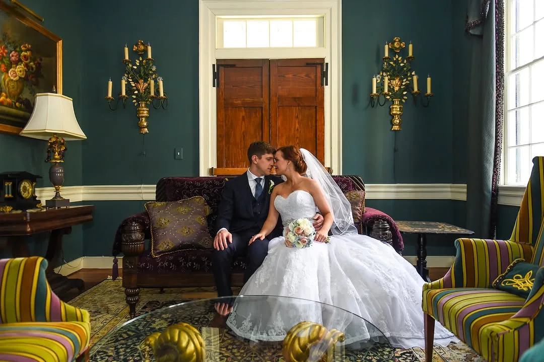 Bride and groom embracing on a velvet antique couch inside The Riddick House, featuring dark teal walls and unique, colorful furniture, perfect for an intimate Fredericksburg wedding.