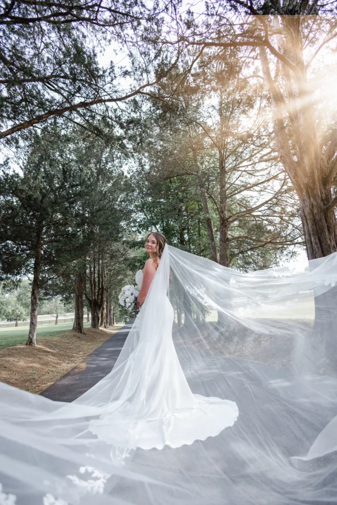 Stunning bridal portrait with the cathedral veil dramatically flowing behind the bride, perfectly backlit by sunlight shining through the trees at Stevenson Ridge, captured by Xpression Photography.