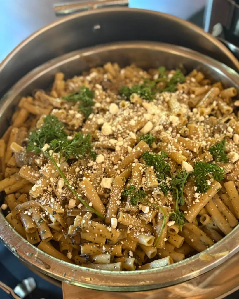 Close-up of rigatoni pasta with a creamy sauce, topped with grated cheese and fresh parsley in a large silver chafing dish, representing an Italian option for a Stevenson Ridge wedding buffet.